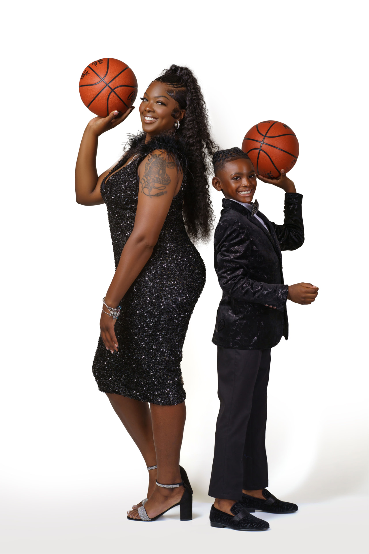 The founders of Side By Side Mobile Hoops, a mother and her son, standing back to back in matching black formalwear, each holding a basketball raised to their own height.
